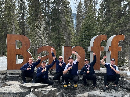 Six curling members show off their medals with Banff sign behind them
